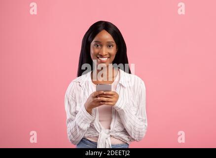 Portrait of smiling young black woman browsing web on smartphone Stock Photo
