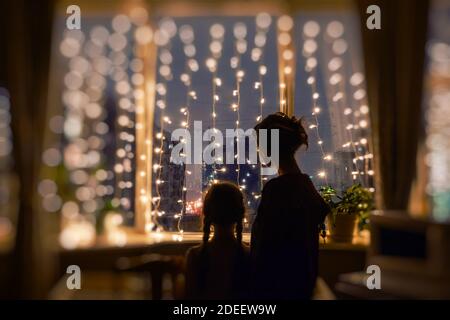 Mother and daughter together standing in the evening, watching the window lights, christmas mood Stock Photo