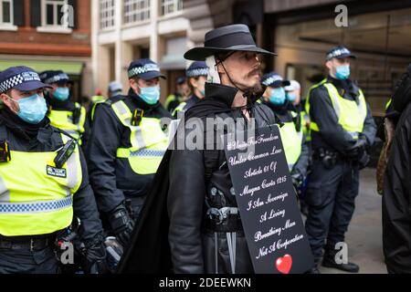 Anti-lockdown protest, Regent Street, London, 28 November 2020. A protester in Guy Fawkes costume stands in front of a line of police officers. Stock Photo