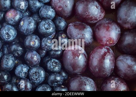 Close-up of a group of blueberries in the middle of the image and another group of black grapes. Split-screen. Fruit and health. Stock Photo