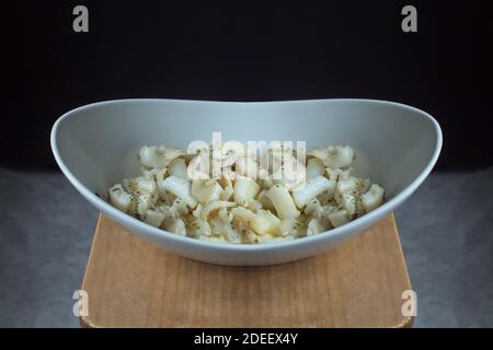 An elegant sinuous shaped ceramic plate filled with delicious cuttlefish food with garlic and green sauce on a vintage wooden table on a marble floor. Stock Photo