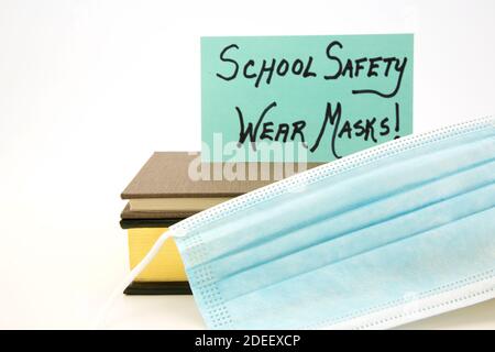 Blue card indicates SCHOOL SAFETY rule is WEAR MASKS.  Covid mask placed with books on white background. Stock Photo