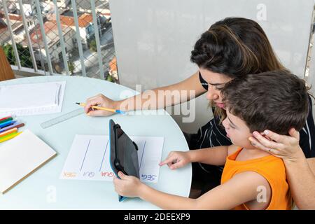 Loving mother helping her son in online classes (during the coronavirus pandemic). Stock Photo
