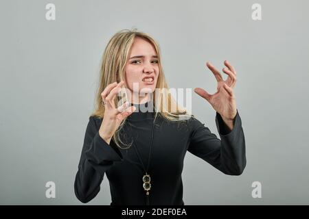 Claw hands, hand gesture and sign, scary desperate, showing claws, nails, making silly face. Young attractive woman, dressed black sweater with green eyes, blonde hair, background Stock Photo