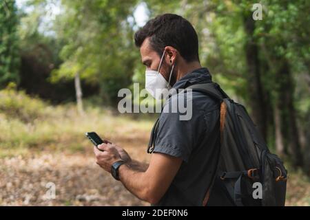 Young man consulting his mobile phone in the mountains. With a mask by the covid-19, carrying a backpack. Concept of sport. Stock Photo