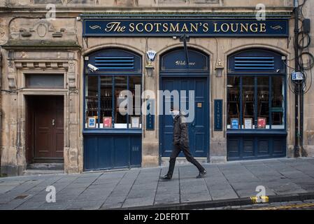Man with a face mask walking past a public house closed because of covid-19 restrictions in Edinburgh, Scotland, UK. Stock Photo