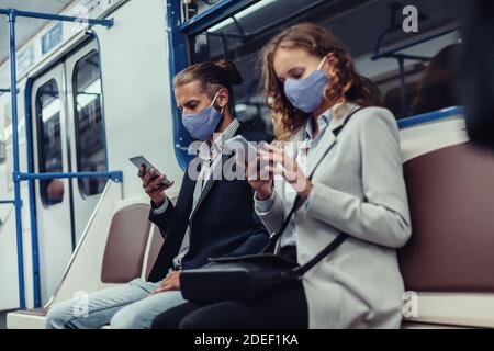 passengers wearing protective masks using their smartphones while sitting in a subway car. Stock Photo
