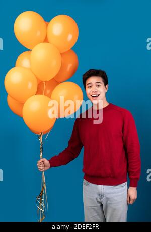 Smiling asian guy holding bunch of yellow balloons Stock Photo