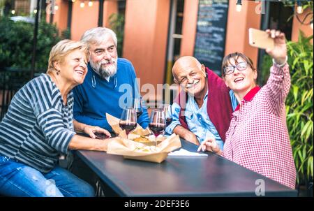 Happy senior friends taking selfie at restaurant - Retired people having fun together with mobile phone - Positive elderly lifestyle concept Stock Photo