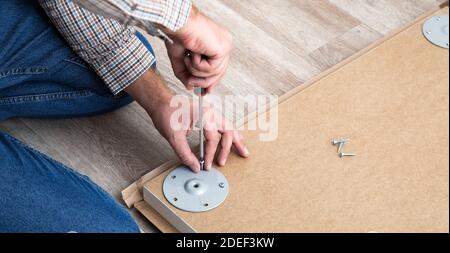 Male hands master collects table furniture using screwdriver tools, instrument at home. Furniture assembly using screwdriver. Moving, home improvement Stock Photo