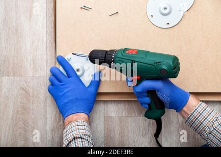 Man in gloves assembles table furniture with drill. Assembly, furniture repair home master. Male hand with drill on floor. Top view Stock Photo