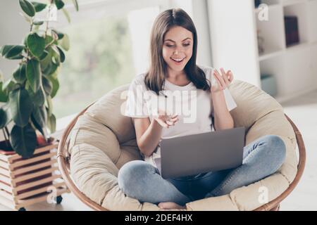 Full size photo of positive girl video chatting on laptop speak sit wicker chair in house living room Stock Photo