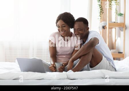 Happy black couple sitting on bed, watching movie on laptop Stock Photo