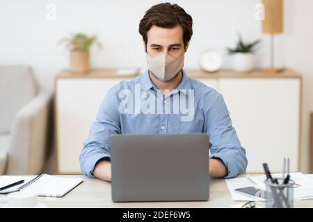 Businessman Wearing Face Mask Working On Laptop Sitting At Workplace Stock Photo