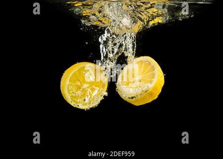 Fresh yellow lemon halves in water splashing isolated on black background. Stock Photo