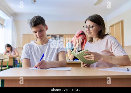 Lesson in class of high school students, female teacher sitting at desk with student Stock Photo