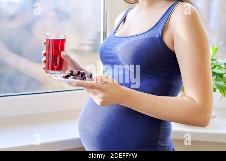 Young beautiful pregnant woman drinking berry juice from glass at home near window Stock Photo