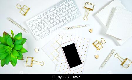 Stylish white and gold theme desktop workspace with keyboard, notebooks and smart phone. Top view blog hero header creative composition flat lay. Stock Photo