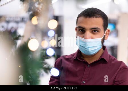 Cheerful African American male in good mood looking at camera and smiling indoors near christmas glowing decorated tree with lights and feeling happy Stock Photo