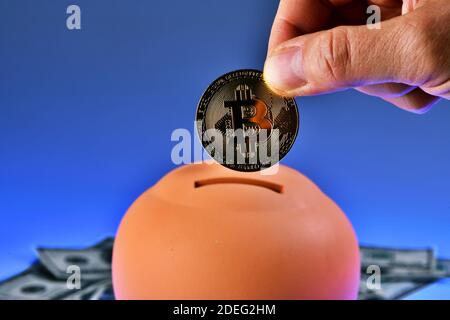 Terracotta piggy bank - money box - isolated on blue background. Saving one Bitcoin in a piggy-bank. cryptocurrency saving Stock Photo