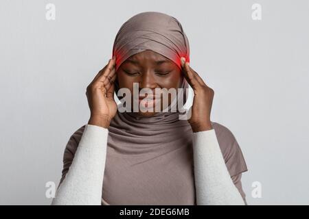 Migraine Concept. Black muslim woman suffering from headache, massaging red sore temples Stock Photo