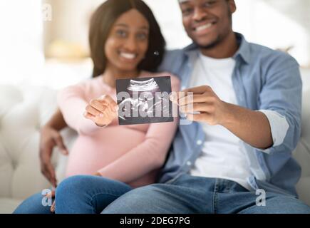 Young future parents holding photo of their unborn baby at home, selective focus on hands Stock Photo