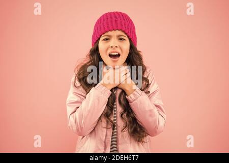 she has sore throat. cold climate weather. happy little girl pink background. kid puffer jacket and knitted hat. winter shopping. how to dress warm in winter. ready for cold winter. no flu. Stock Photo