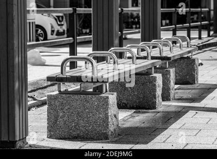 A black and white picture of a bench, resting on roughly hewn stones, with shiny chrome handels/bars on a sunny day. Stock Photo