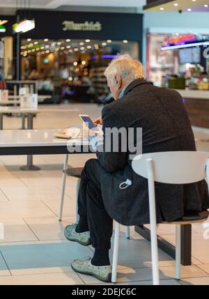 Back view of an old man sitting in a cafeteria and using his smartphone. Side view. Stock Photo