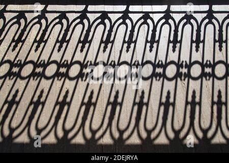 High Angle View of the Reflection of Wrought-Iron Balcony Decoration on a Sunlit Wooden Floor Stock Photo