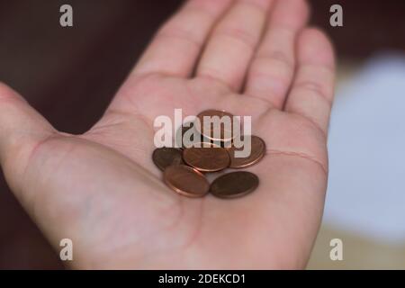 Persons hand holding out a a handful of United States of America (USA) pennies, a useless coin on a brown background. Money exchange. Selective Focus Stock Photo