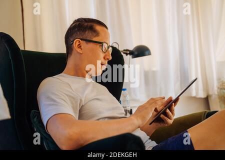 Close up of young man reading with digital tablet while sitting on his sofa couch in living room at home Stock Photo