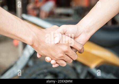 close up of both hands shaking hands against the background of the motorbike in the tire repair shop Stock Photo