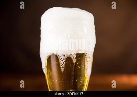 Golden cold beer in the glass on the table with overyflow frothy foam Stock Photo