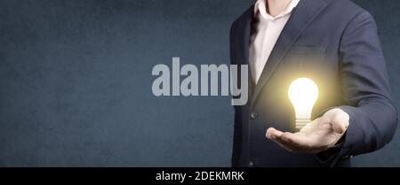 Idea concept. businessman holds a glowing light bulb in his hand on blue background. idea, innovation and inspiration concept. banner, copy space Stock Photo