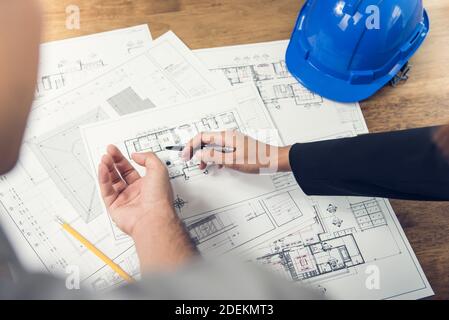 Engineer and architect team discussing floor plan layout for new development in progress on site with blue safety helmet on table Stock Photo