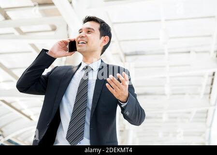 Thai Asian Businessman walking while holding and talking on mobile phone happily in the city on the way to work at the office Stock Photo