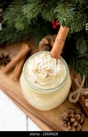 Traditional Christmas eggnog drinks with whipped cream, ground nutmeg, cinnamon and decorating items on wood table, preparing for celebrating festive Stock Photo