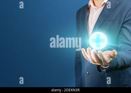 businessman hand holding medicine sign. man holds a glowing medical cross sign in his hand. Concept of health insurance and medical care. copy space. Stock Photo