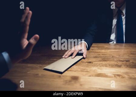 Businessman rejecting money in the envelope given by his partner in dark private room - anti bribery concept Stock Photo