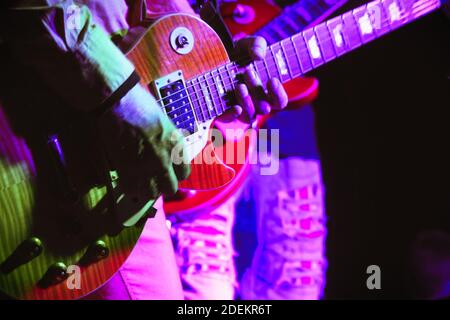 Guitar in the hands of a guitarist standing on stage in the spotlight. Soft focus Stock Photo