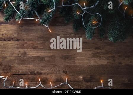 Blinking Christmas decorative light string with green pine leaves on wood table background, top view border design with copy space Stock Photo