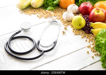Colorful healthy medicinal fruits, vegetables, spices and nuts on white wood background with stethoscope  - food and medical concept Stock Photo