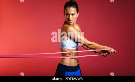 fitness women doing resistance workout with focus. Woman doing core strength training using resistance band on maroon background. Stock Photo
