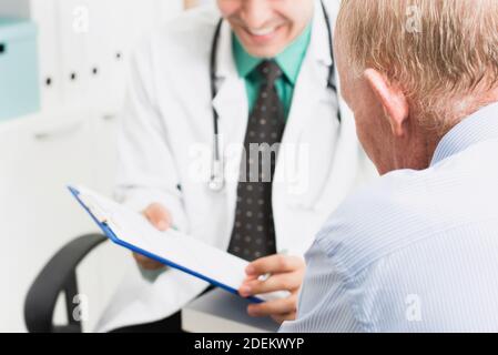 Senior male patient looking at medical record while consulting with kind friendly smiling doctor in hospital Stock Photo