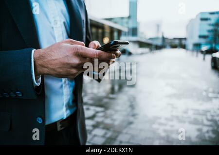 Close up of mixed race businessman texting on mobile device standing outside office block Stock Photo
