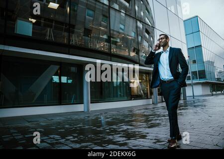 Portrait of mixed race businessman chatting on cellular device while walking to work in office block Stock Photo