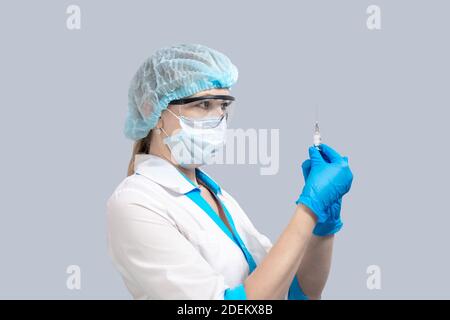 nurse on a gray background in a protective mask and glasses, holds a syringe with a vaccine. Medicine and healthcare. Coronavirus treatment. Stock Photo