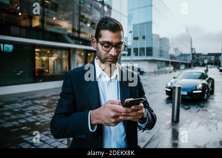 Mixed race businessman texting on smartphone dressed smartly while walking to work in office block Stock Photo