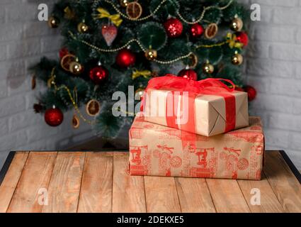 Beautiful Christmas gift boxes on the wooden table next to the Christmas tree in the room. Red ribbon Stock Photo